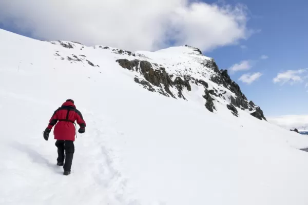 Hiker crossing snow below mountain peaks